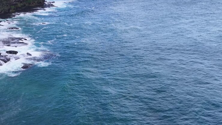 Drone che sorvola la costa rocciosa, catturando le onde blu dell'oceano e le scogliere costiere frastagliate