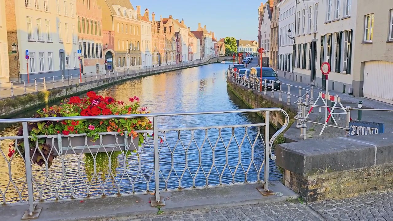 Scena sul lungomare di Bruges, Belgio, con canale, ringhiera di ponte in ferro, fiori colorati, architettura medievale, riflessi e luce dell'ora d'oro, un pittoresco paesaggio urbano europeo