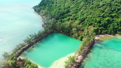 Beautiful-turquoise-lagoon-for-children-to-swim,-surrounded-by-rocks-and-tropical-plants-near-shore-of-island-with-lush-vegetation-in-Thailand