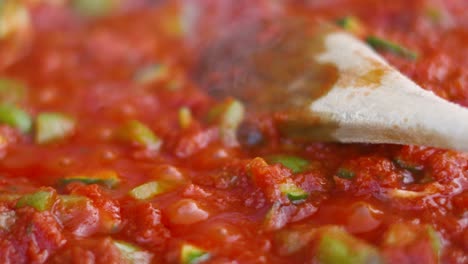 italian tomato passata bubbling in slow motion in frying pan being cooked outside with wooden spoon lying gently on top with lots of vegetables and herbs 4k