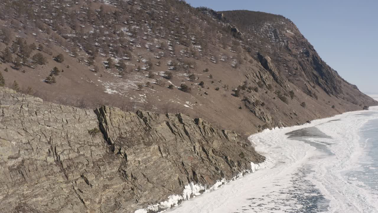 겨울에 얼어붙고 얼음으로 인 바이칼 호수의 바위가 있는 연안에서 드론이 날아다니는 순환 비행입니다.