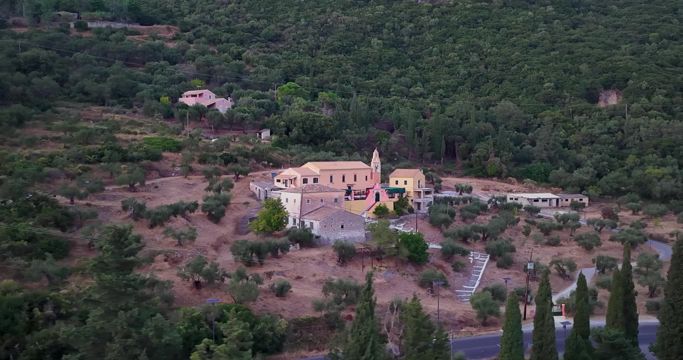 Ampia vista aerea del Monastero Ortodosso di Panagia Vlacherna a Skripero, Corfù, circondato da rigogliose colline verdi e uliveti al crepuscolo