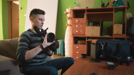 person seated in home studio, assembling camera equipment with microphone and lenses on table. preparing for video shooting, surrounded by colorful background and various objects