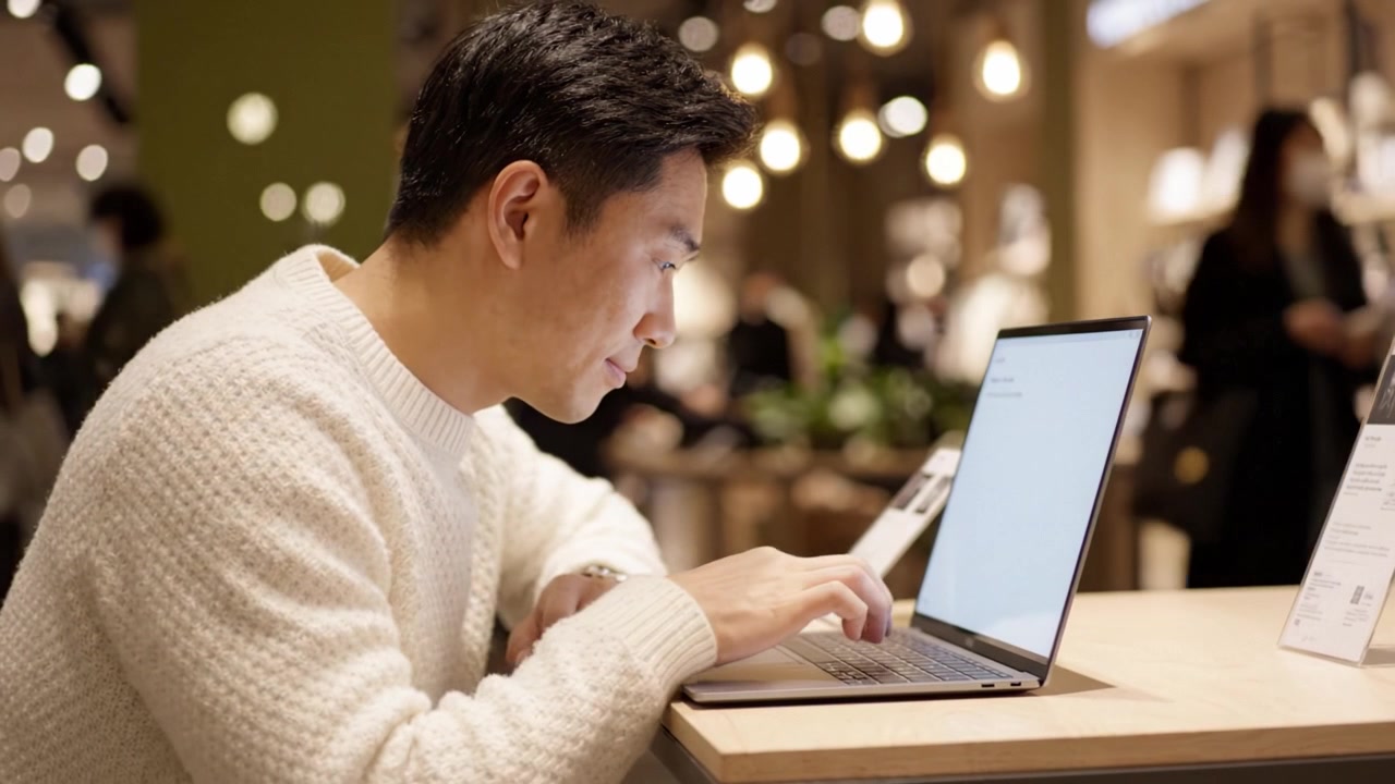 スタイリッシュな小売空間でノートパソコンに集中し、仕事に没頭する若者。テクノロジーと現代のショッピングを融合したモダンな環境を表現