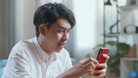 Close Up Side View Of Happy Asian Man Celebrating While Using Smartphone In The Living Room