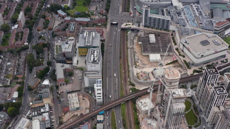 Aerial-view-of-busy-multilane-road-leading-along-construction-site-of-development-project.-Tilt-down-footage-to-railway-bridge.-London,-UK