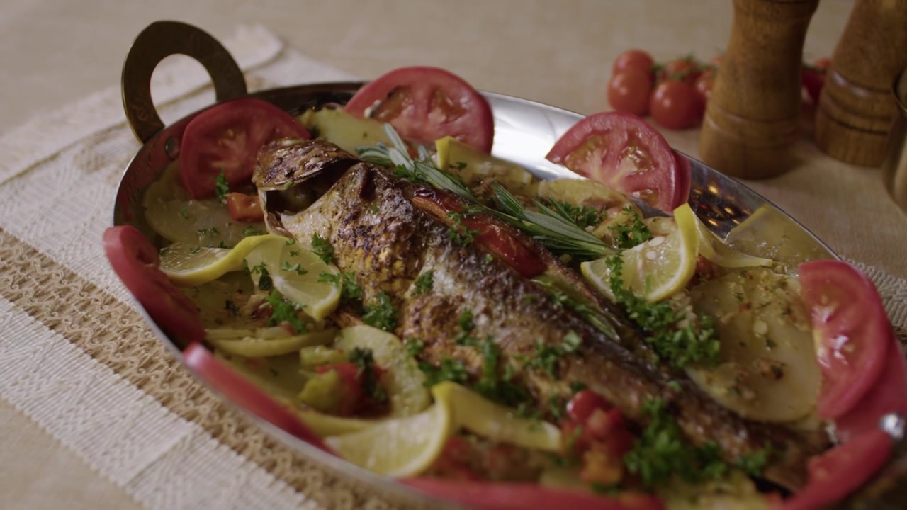 Peixe inteiro assado guarnecido com limão, tomate e ervas em uma bandeja tradicional