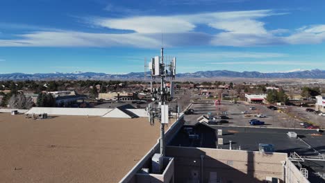 tomada aérea de un dron que muestra una rotación de 360° alrededor de una torre celular montada en un edificio minorista, destacando su tecnología e integración con la estructura.