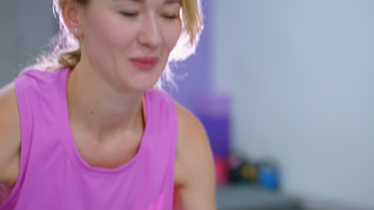 primer plano de una mujer sonriendo mientras hace ejercicio, empujando hacia adelante, con la luz iluminando su cara y una vista parcial de la pierna de otra persona cercana en un entorno de gimnasio