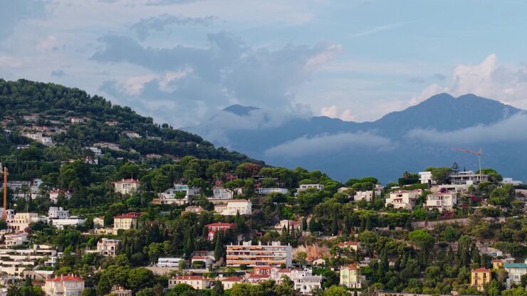Drone si alza lateralmente oltre le case sulla collina della Riviera sotto nuvole drammatiche