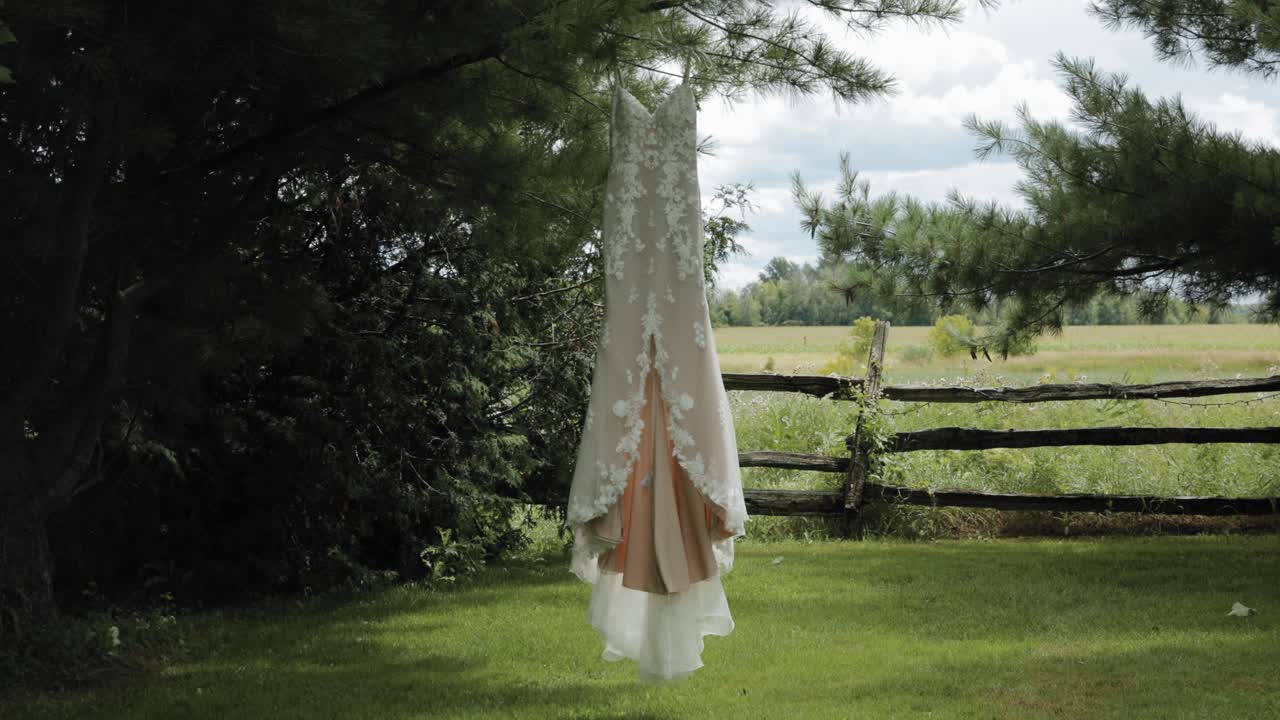 Beautiful designer wedding gown swaying in the breeze as it hangs from a pine tree in the back yard at the Strathmere Wedding and Event Centre