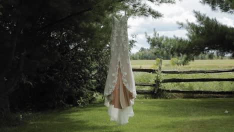 beautiful designer wedding gown swaying in the breeze as it hangs from a pine tree in the back yard at the strathmere wedding and event centre