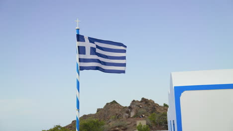 a greek flag flies in the wind in santorini