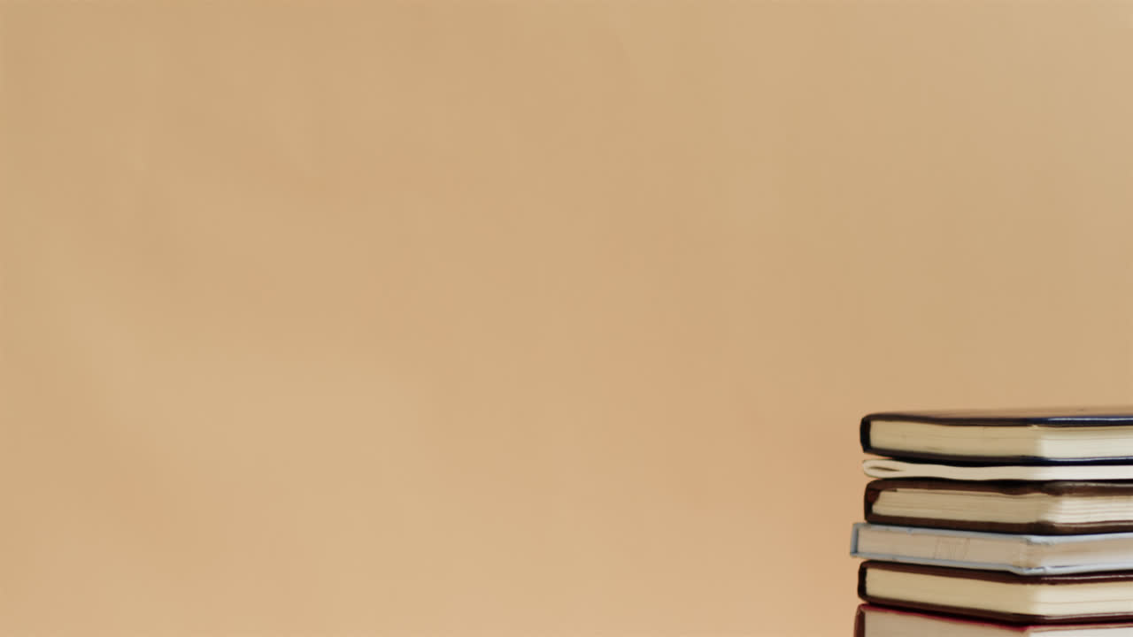 Close up of stack of books with copy space on beige background, in slow motion