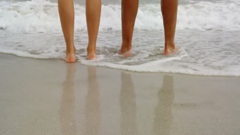 Low-section-of-couple-standing-barefoot-on-the-beach-4k