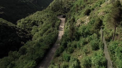 Vista-Aérea-Hacia-Delante-De-Una-Carretera-Con-Túnel-En-Las-Montañas-Salvajes