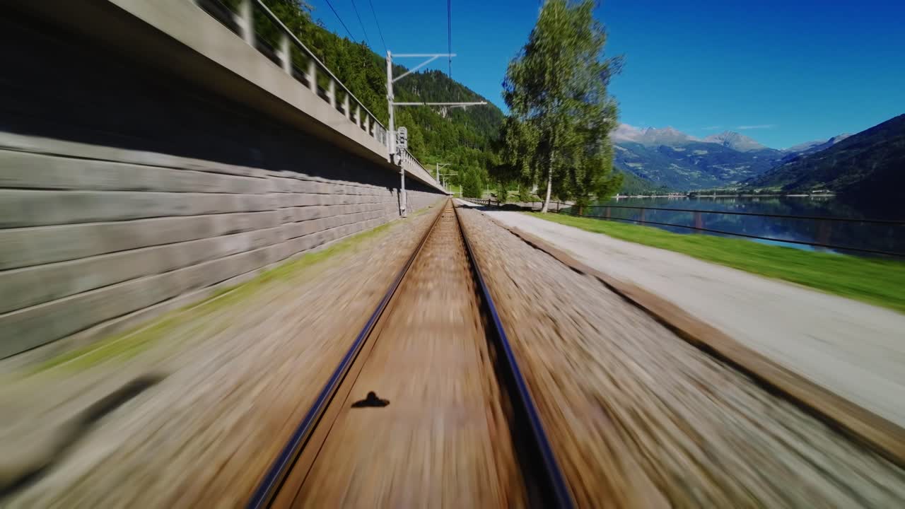FPV flight joining railway tracks, following the line at low altitude, then leaving the rails and flying back over the lake with mountains in the background