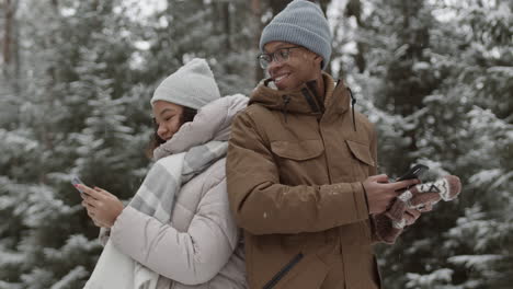 couple using phones in a snowy forest