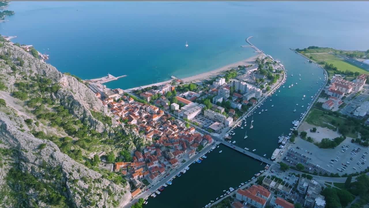 크로아티아 의 오미스 시 와 산 들 과 아드리아 해 로 둘러싸인 중세 시대 의 지붕 을 연결 하는 세티나 강 다리 의 영화적 인 항공 전망