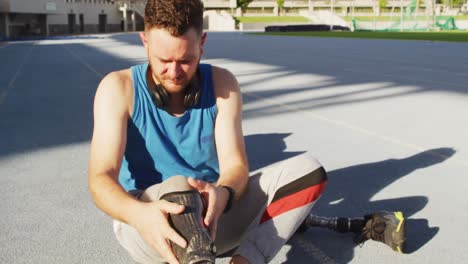 caucasian disabled male athlete sitting, putting on running blade