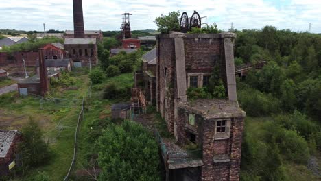 abandoned old overgrown coal mine industrial rusting wheel buildings aerial view close orbit right