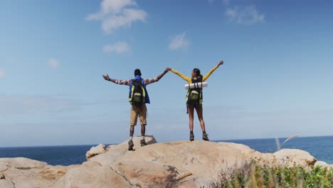 vista trasera de una pareja afroamericana de pie en las rocas con los brazos abiertos mientras trekking