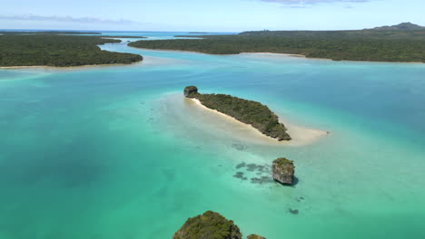 upi bay, isle of pines and islets in the turquoise water - pull back aerial flyover