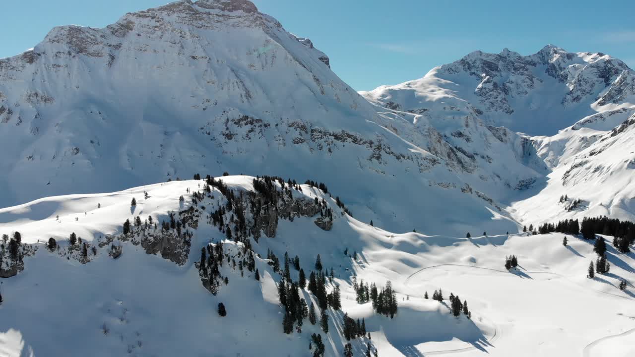Panoramic drone view of several mountain ranges and trees in Warth, a small municipality in Vorarlberg, Austria on a clear sunny day with beautiful blue skies in 4K