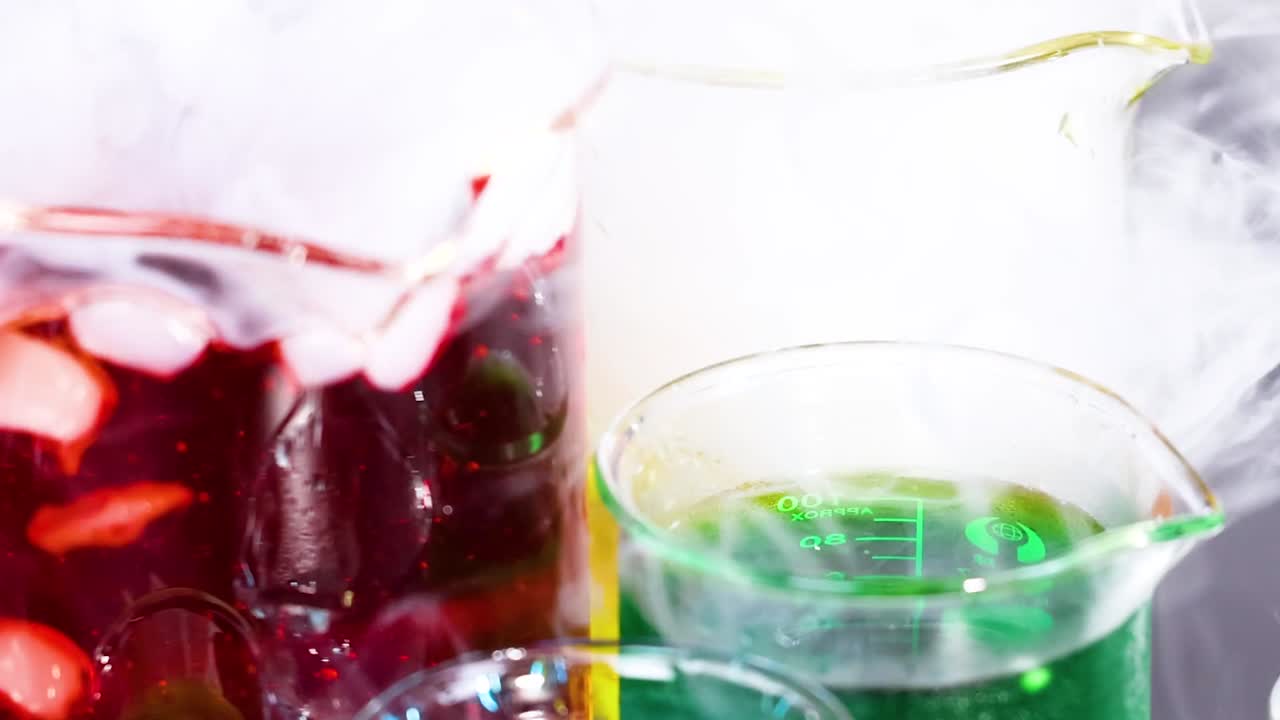 Close-up of red and green liquids in beakers with swirling smoke effects.