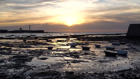 slow cinematic tilt up over small fishing boat silhouettes at low tide at ocean