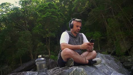 man sitting on rocks with headphones on and looking at phone