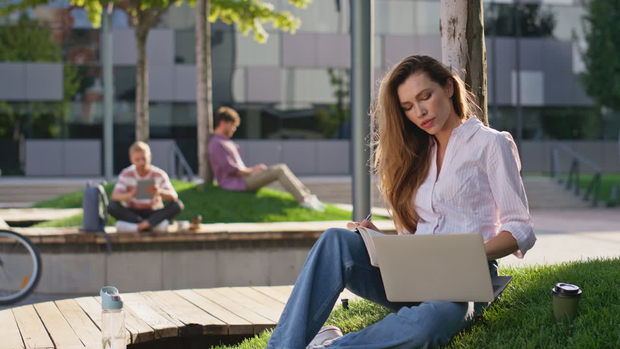 Byfolk arbejder på bærbare computere i park. Smilende kvindelig freelancer holder pause.