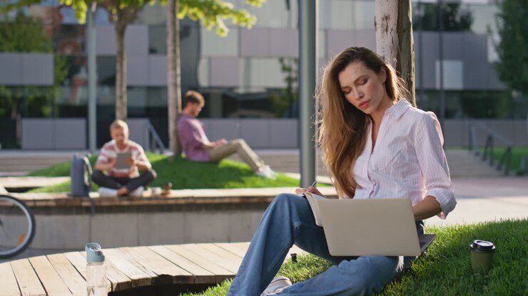 Persone in città che lavorano con i portatili in un parco. Donna freelance sorridente che si prende una pausa
