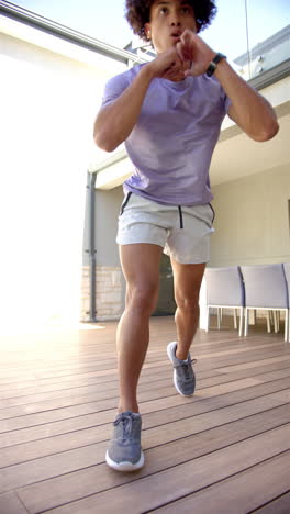 vertical video: young biracial male homeowner exercising on wooden deck