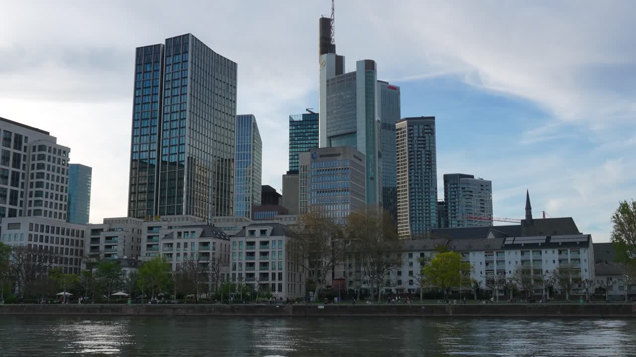 Skyline des Frankfurter Finanzviertels, tagsüber vom Main aus gesehen, mit modernen Wolkenkratzern und Gebäuden am Flussufer.