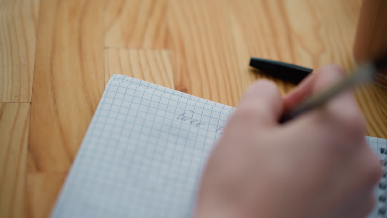 펜으로 글을 쓰는 사람의 가까운 손으로 보는 모습, 부분적으로 펜 개와 나무 테이블에 차 컵을 보여주는 모습, 글을 쓰면서 집중과 상을 전달합니다.