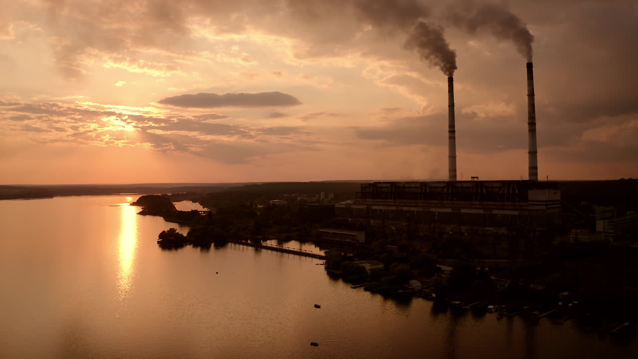 Factory with smoke pipes in evening nature. Dangerous manufacturing pollute atmosphere. Industrial plant near the river at dusk. Ecological problems.