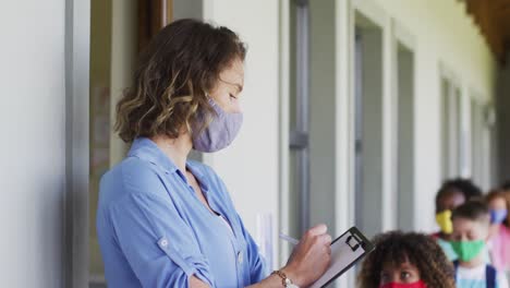 Female-teacher-wearing-face-mask-writing-on-clipboard