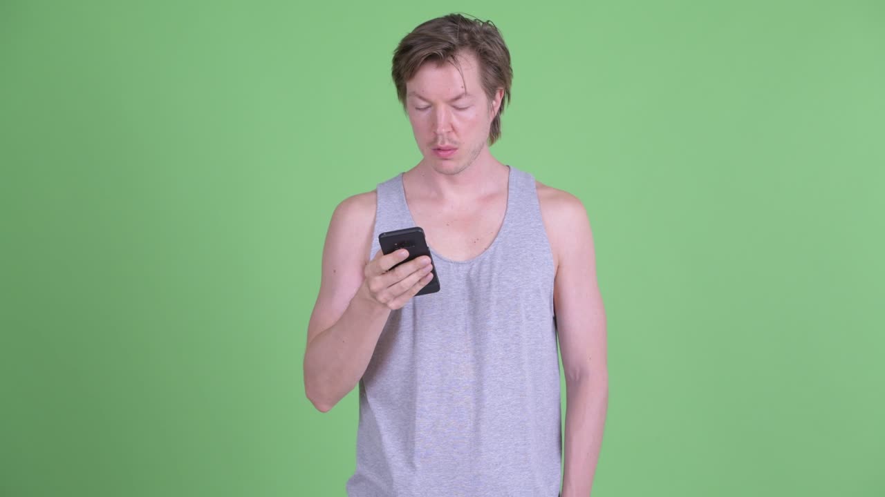 녹색 스튜디오 배경 에 휴대 전화 를 사용 하는 동안 우울 한 모습 을 보이는 백인 남자 의 초상화