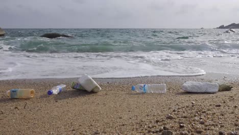 Rauschende-Welle,-Die-Plastikmüll-Zum-Strand-Schiebt,-Paralleler-Statischer-4k-Seitenschuss-Mit-Niedrigem-Winkel