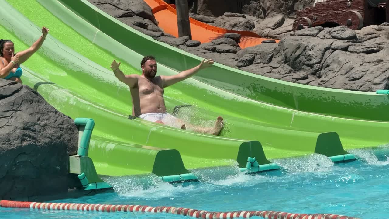 los aventureros se deslizan por un vibrante agua verde deslizarse en una piscina brillante en un parque acuático animado