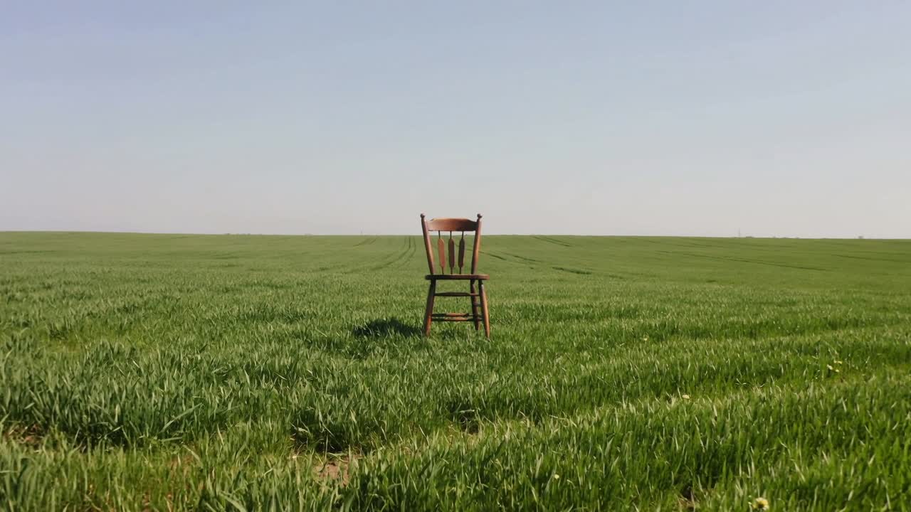 La telecamera che si avvicina, facendo apparire più grande una singola sedia di legno in un campo verde, mostrando le tracce del trattore.