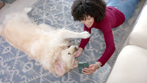 Happy-biracial-woman-taking-photo-with-golden-retriever-dog-using-smartphone-at-home,-slow-motion