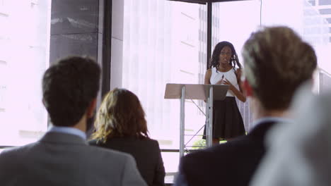 Audience-at-seminar-applauding-young-black-woman-at-lectern,-shot-on-R3D