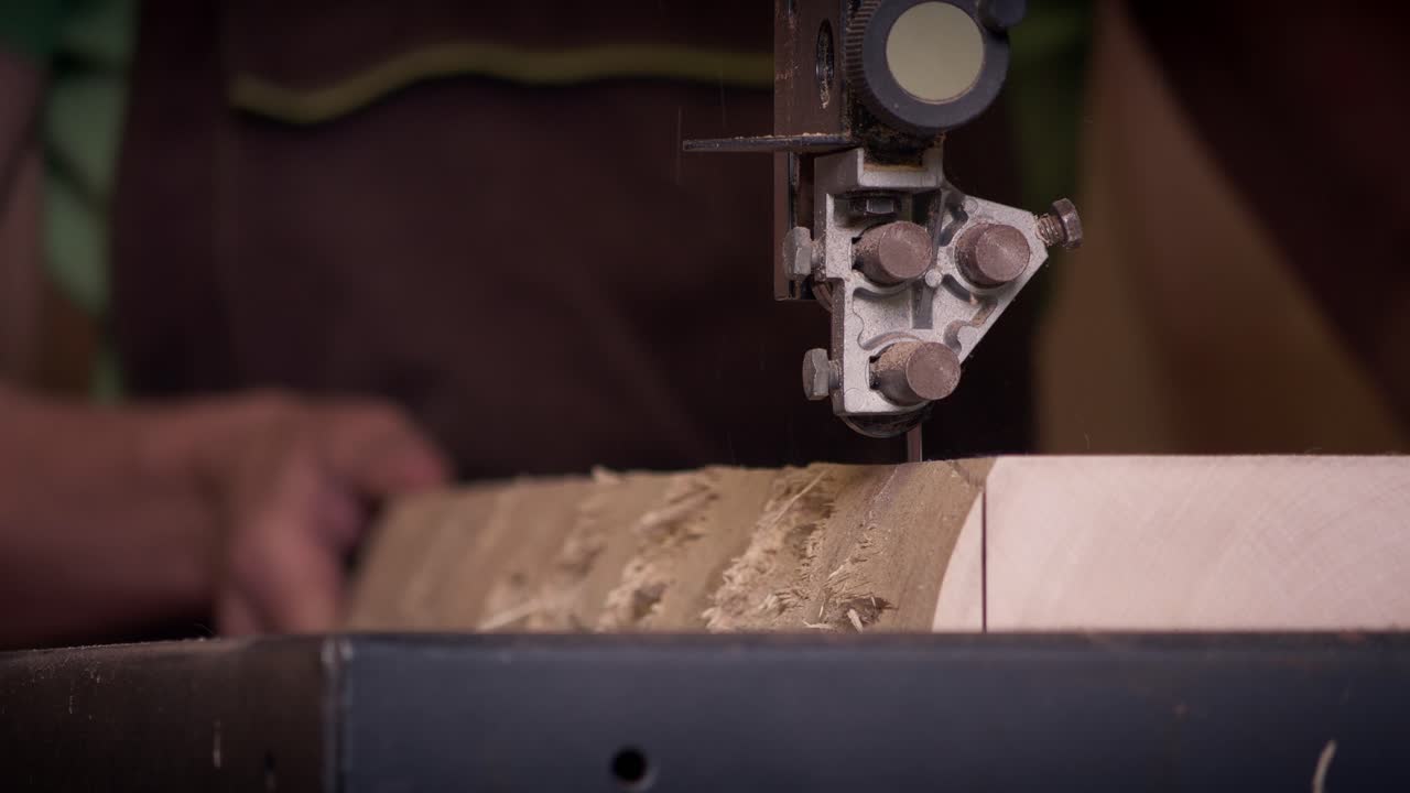 Heavy duty bandsaw blade slices into a thick block of light wood in a professional carpentry shop. Slow motion capture of industrial woodworking machinery in action