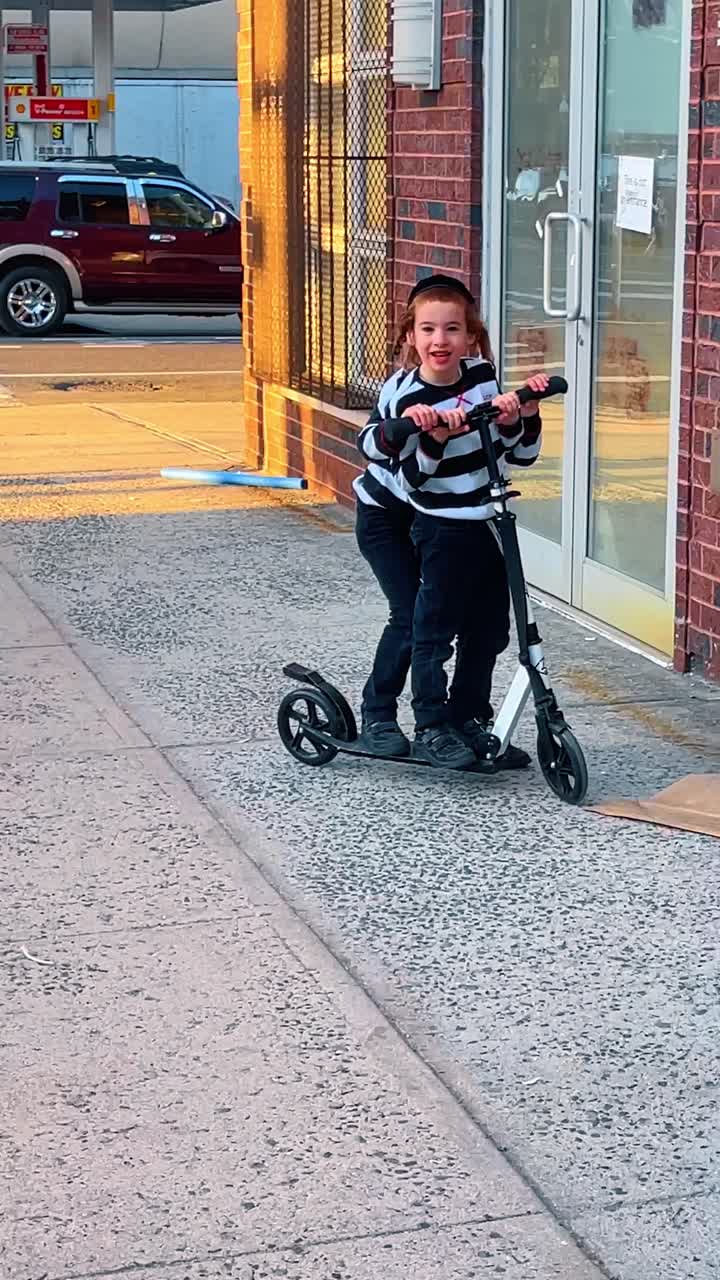 New York, ABD, 11 Mayıs 2025: Geleneksel Yahudi kıyafetli iki erkek çocuğu kaldırımda scooter sürüyor. Çizgili tişörtlü ve kippalı çocuklar şehirde beyaz scooter ile oynuyor