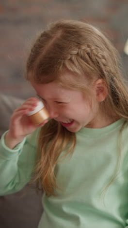 joyful little girl shakes bottle with golden glitter sitting on sofa in living room slow motion. supplies for art craft. development hobby for children