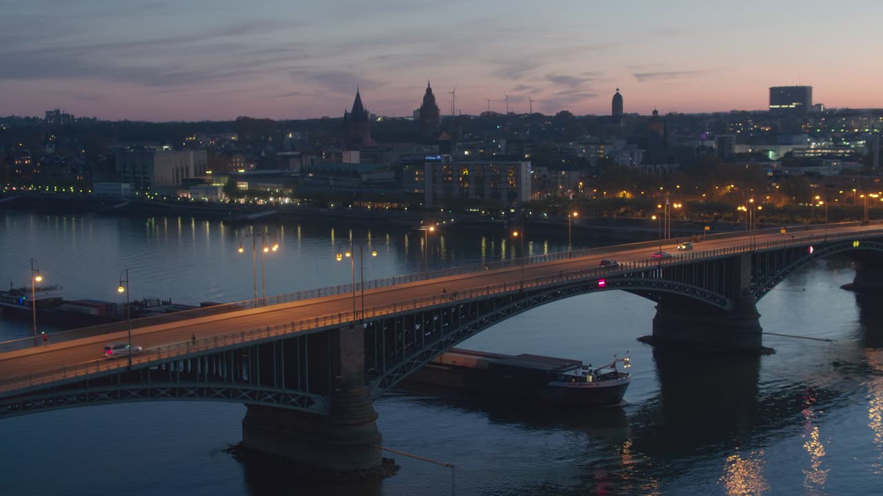 Ripresa aerea con drone al tramonto della città di Magonza di notte, con un drone sopra il vecchio ponte e una nave sul fiume Reno.