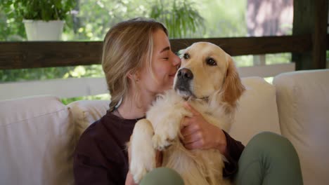 A-blonde-girl-in-a-dark-red-sweater-sits-on-a-sofa-in-nature-and-hugs-and-strokes-her-light-colored-dog