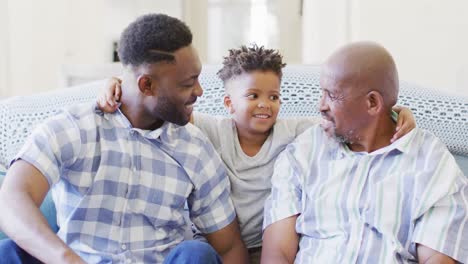 Smiling-african-american-son-between-happy-father-and-grandfather-on-couch-at-home,-slow-motion